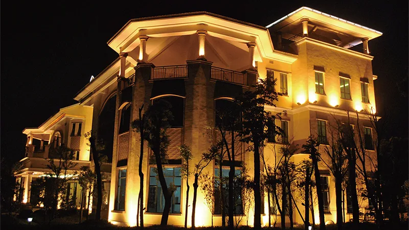 Fachada de tres plantas iluminada desde el suelo de noche, con la caída de luz hacia las plantas superiores