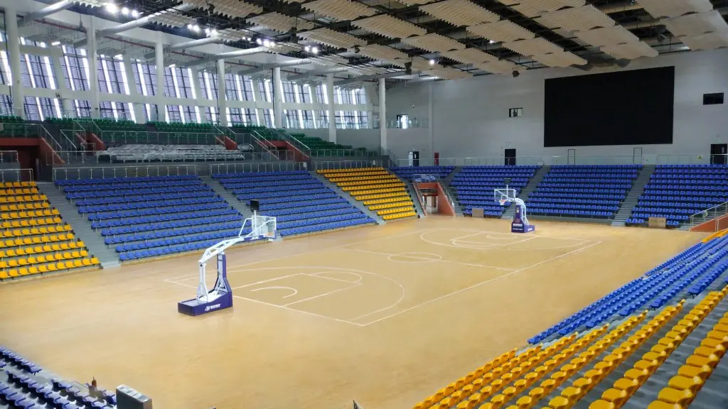 Indoor sports hall with a lit playing surface, seating on three sides and roof structure above